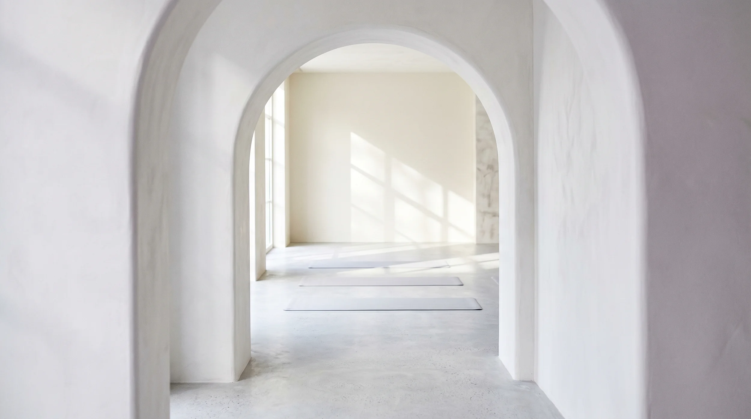 A bright, minimal practice room with three mats on the floor